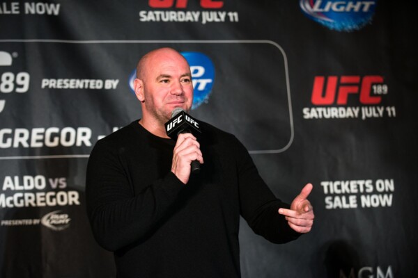 Dana White w czarnym swetrze stoi na tle baneru konferencyjnego UFC