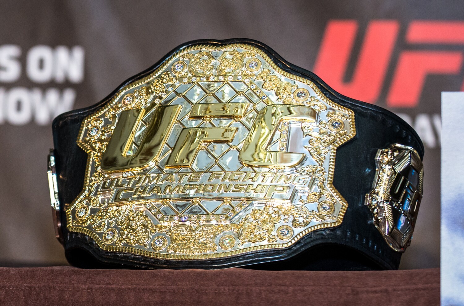 Pas UFC leżący na stole podczas konferencji prasowej. W tle banda z logotypem UFC.