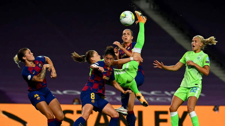 Ewa Pajor w jaskrawozielonym stroju VfL Wolfsburg wyskakuje do piłki w otoczeniu zawodniczek FC Barcelony podczas meczu Ligi Mistrzyń.