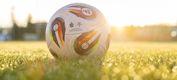 Zdjęcie przedstawia oficjalną piłkę meczową Konektis Pro, stworzoną przez firmę Adidas na sezon 2025/2026 PKO Bank Polski Ekstraklasy. Piłka leży na świeżej, pokrytej rosą murawie, a w tle widoczne są rozmyte promienie porannego słońca, podkreślające nową erę technologii na polskich boiskach.