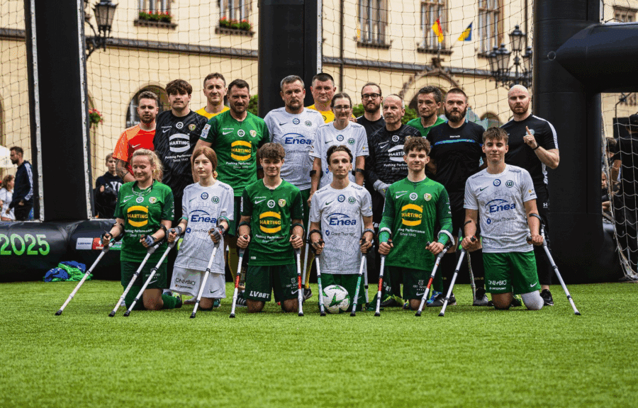 Grupowe zdjęcie drużyny Amp Futbolu Warty Poznań na boisku podczas wydarzenia plenerowego we Wrocławiu, zawodnicy w strojach sportowych z kulami, na tle zabytkowych budynków i bramek z napisem "Wrocław Final 2025".