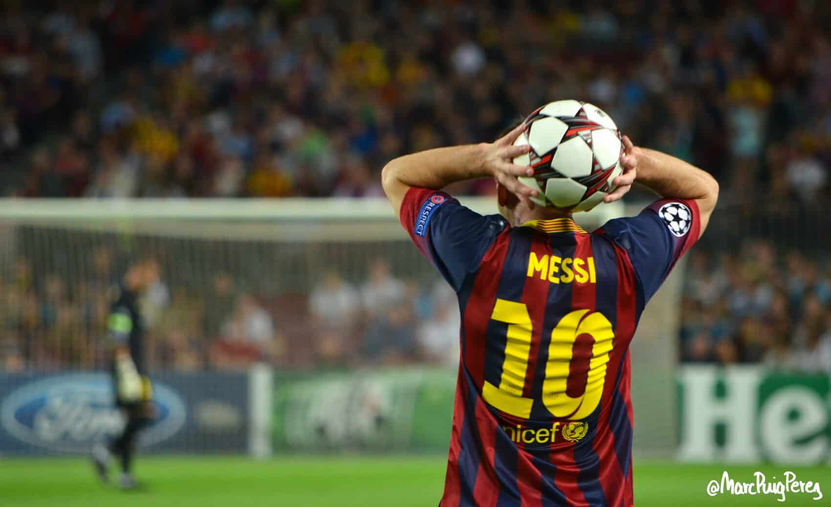 Lionel Messi w koszulce FC Barcelony z numerem 10 wykonuje wrzut z autu podczas meczu piłkarskiego Ligi Mistrzów na stadionie, widok od tyłu, w tle bramkarz i kibice na trybunach