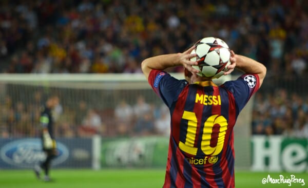 Lionel Messi w koszulce FC Barcelony z numerem 10 wykonuje wrzut z autu podczas meczu piłkarskiego Ligi Mistrzów na stadionie, widok od tyłu, w tle bramkarz i kibice na trybunach