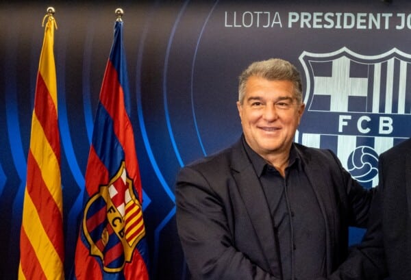 Dwóch mężczyzn w garniturach podaje sobie ręce na tle herbu FC Barcelona i flag klubowych w loży prezydenckiej Camp Nou