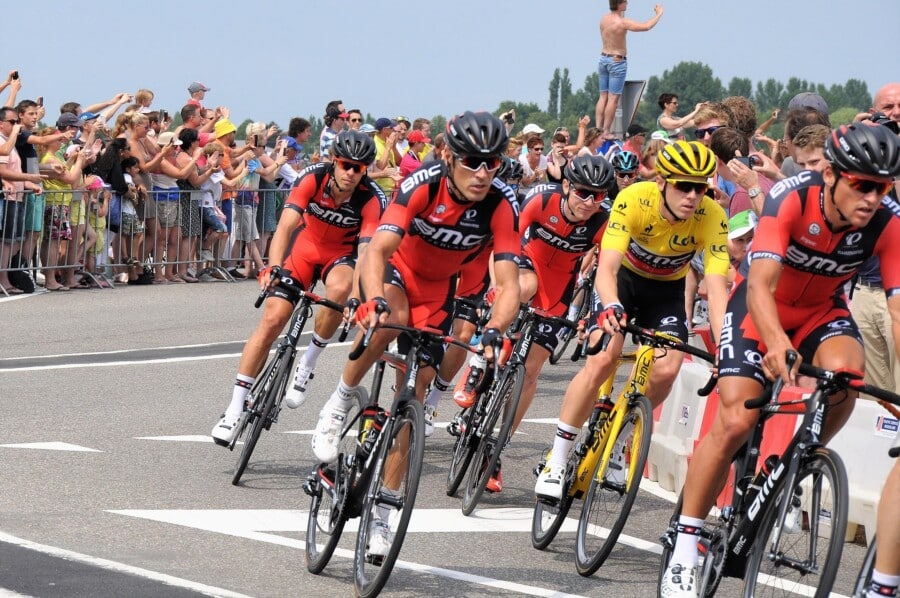 Kolarze drużyny BMC i lider wyścigu w żółtej koszulce rywalizujący podczas etapu Tour de France, kibice dopingujący zawodników przy trasie.