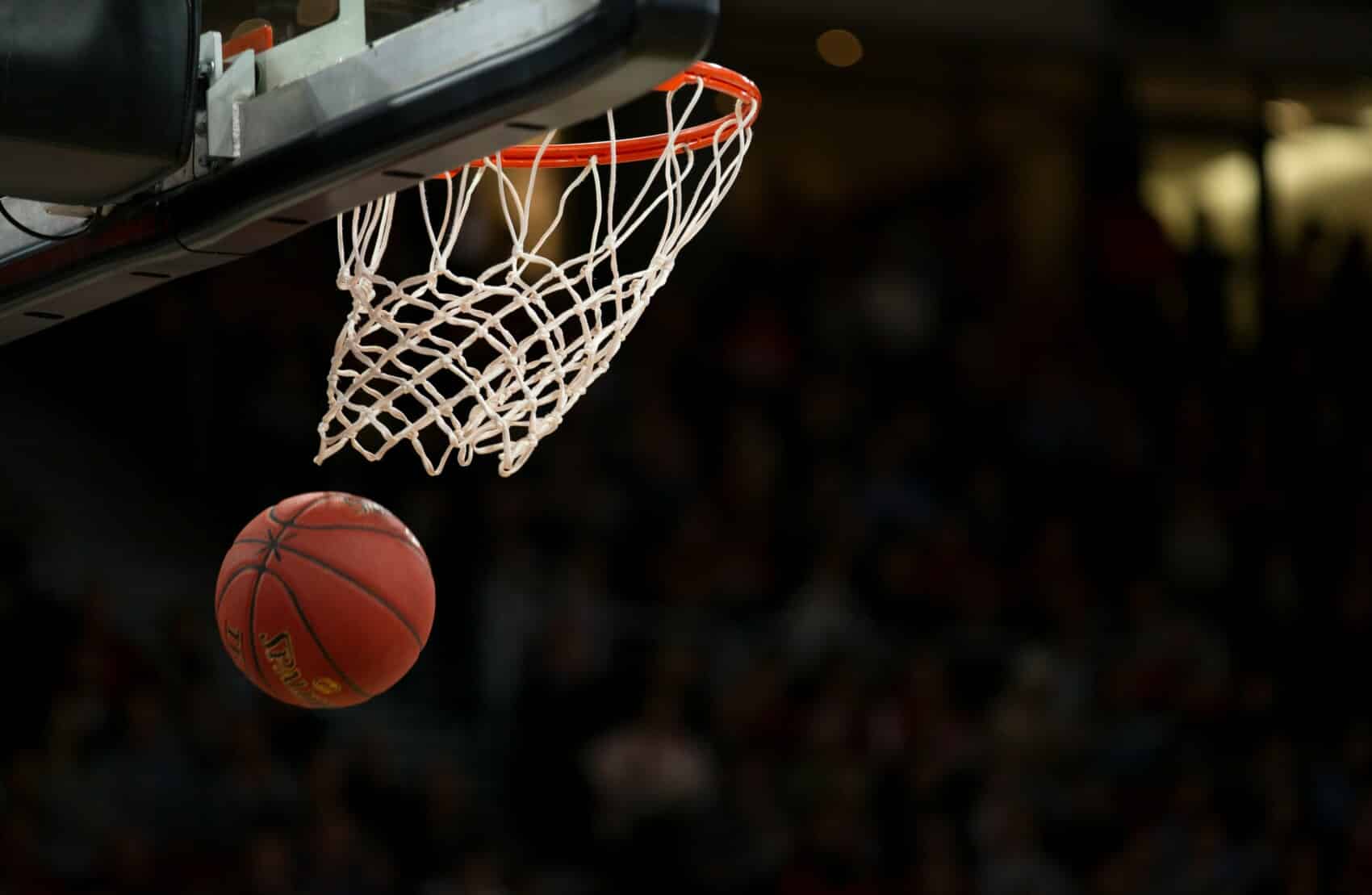 Piłka do koszykówki wpadająca do kosza podczas meczu na hali sportowej.