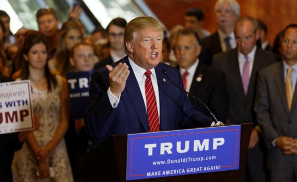 Donald Trump gestykuluje na wiecu wyborczym, stojąc za amboną z napisem Make America Great Again