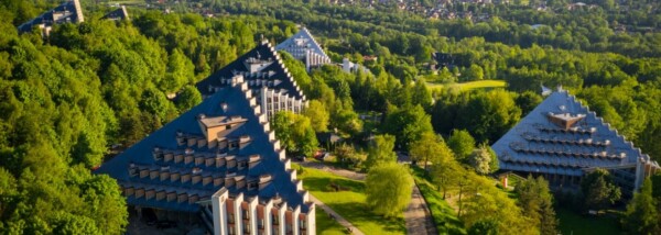 Nowoczesne piramidalne budynki Uzdrowiska Ustroń otoczone zielenią i lasami, widok z lotu ptaka w słoneczny dzień.