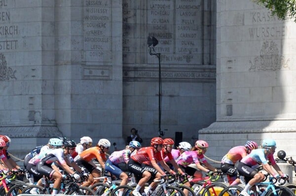 Kolarze biorący udział w wyścigu Tour de France Femmes jadący w zwartej grupie ulicami Paryża na tle Łuku Triumfalnego.