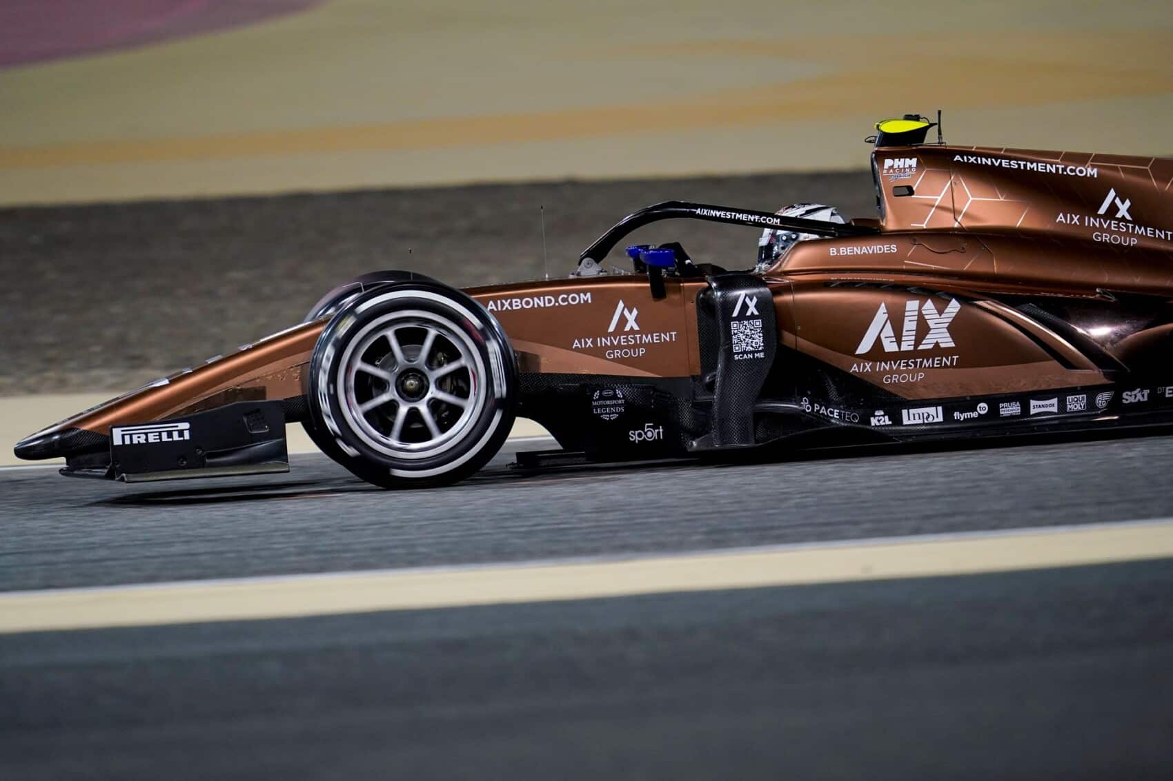 Bolidek zespołu AIX Racing w brązowym malowaniu podczas wyścigu Formuły 2 na torze, widoczny logotyp sponsora i nazwisko kierowcy na nadwoziu.