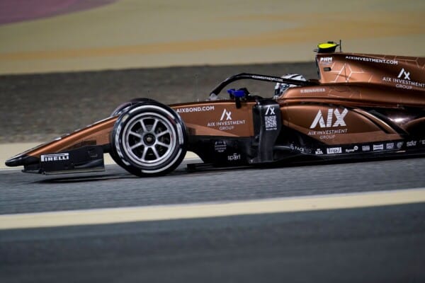 Bolidek zespołu AIX Racing w brązowym malowaniu podczas wyścigu Formuły 2 na torze, widoczny logotyp sponsora i nazwisko kierowcy na nadwoziu.