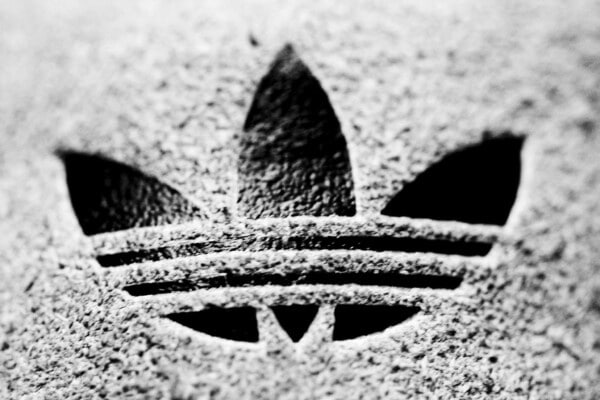 Logo Adidas Trefoil w czarno-białym zbliżeniu, wyryte na fakturowanej powierzchni, symbol kultowej serii Originals