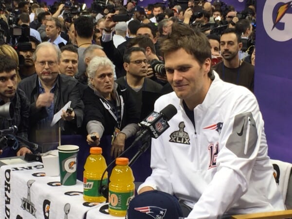 Konferencja prasowa NFL Super Bowl XLIX – zawodnik New England Patriots w białej kurtce, mikrofon NFL Network, napoje Gatorade i tłum fotoreporterów.