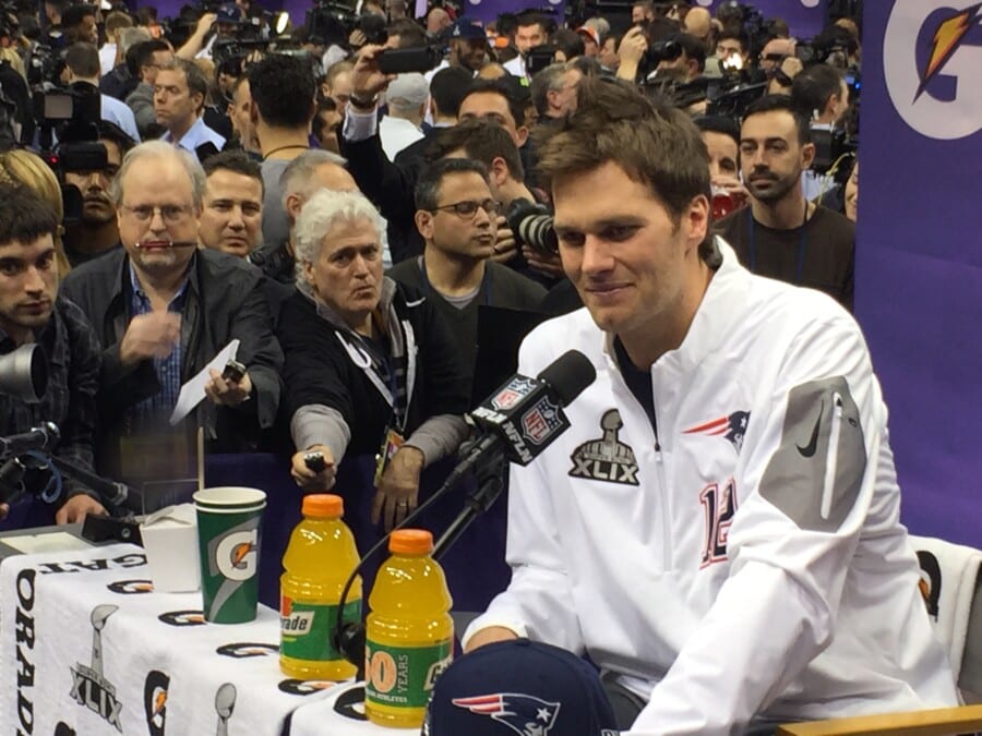Konferencja prasowa NFL Super Bowl XLIX – zawodnik New England Patriots w białej kurtce, mikrofon NFL Network, napoje Gatorade i tłum fotoreporterów.