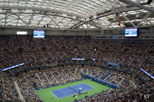 Wnętrze stadionu Arthur Ashe z zamkniętym dachem, widoczne pełne trybuny kibiców oraz kort podczas meczu tenisowego US Open