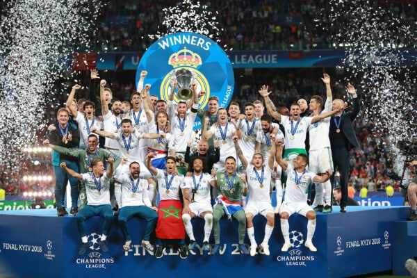 Drużyna Realu Madryt świętuje zwycięstwo w finale Ligi Mistrzów UEFA 2018 w Kijowie, trzymając trofeum na podium otoczonym konfetti.