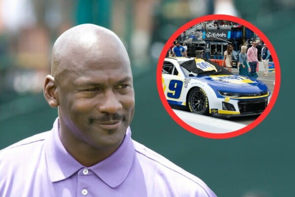 Michael Jordan w fioletowej koszulce polo obok biało-niebieskiego samochodu wyścigowego NASCAR z numerem 9, na torze wyścigowym w otoczeniu ludzi i strefy serwisowej