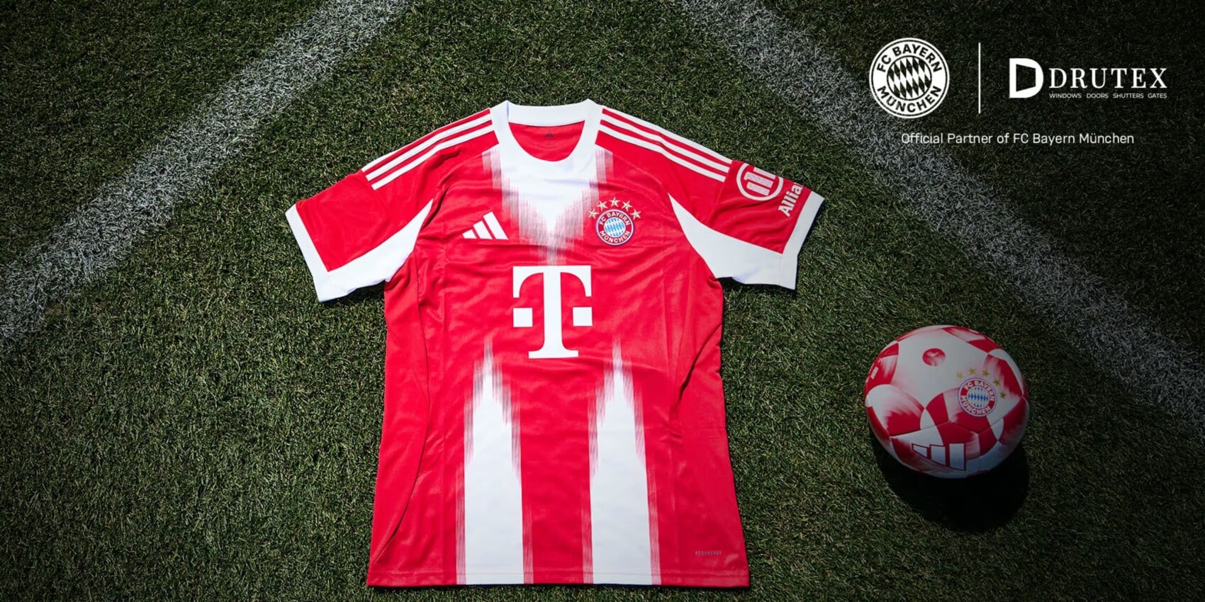 Koszulka domowa FC Bayern Monachium leżąca na murawie boiska wraz z piłką klubową, widoczne logo sponsora DRUTEX i T-Mobile oraz herb klubu.