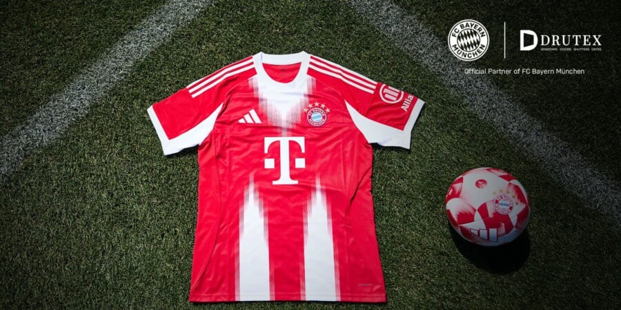 Koszulka domowa FC Bayern Monachium leżąca na murawie boiska wraz z piłką klubową, widoczne logo sponsora DRUTEX i T-Mobile oraz herb klubu.