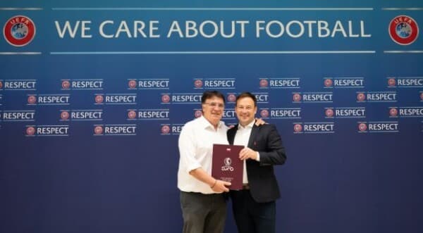 Przedstawiciele PZPN podczas oficjalnej ceremonii z dokumentacją kandydatury UEFA EURO na tle ścianki z logotypami UEFA i hasłem "We care about football"