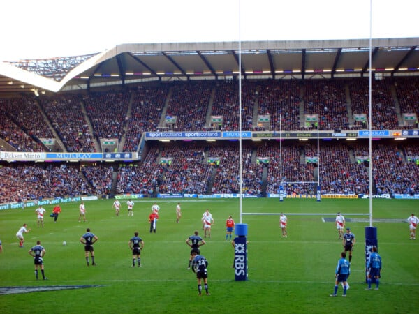 Mecz rugby na stadionie Murrayfield w Edynburgu, zawodnicy na boisku podczas meczu Szkocja vs Anglia, liczne trybuny pełne kibiców.