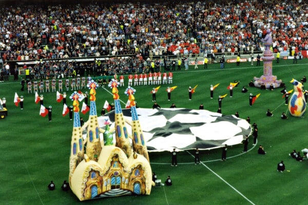 Ceremonia otwarcia finału Ligi Mistrzów UEFA na stadionie piłkarskim; na murawie duża flaga Champions League, kolorowe dekoracje i pełne trybuny kibiców