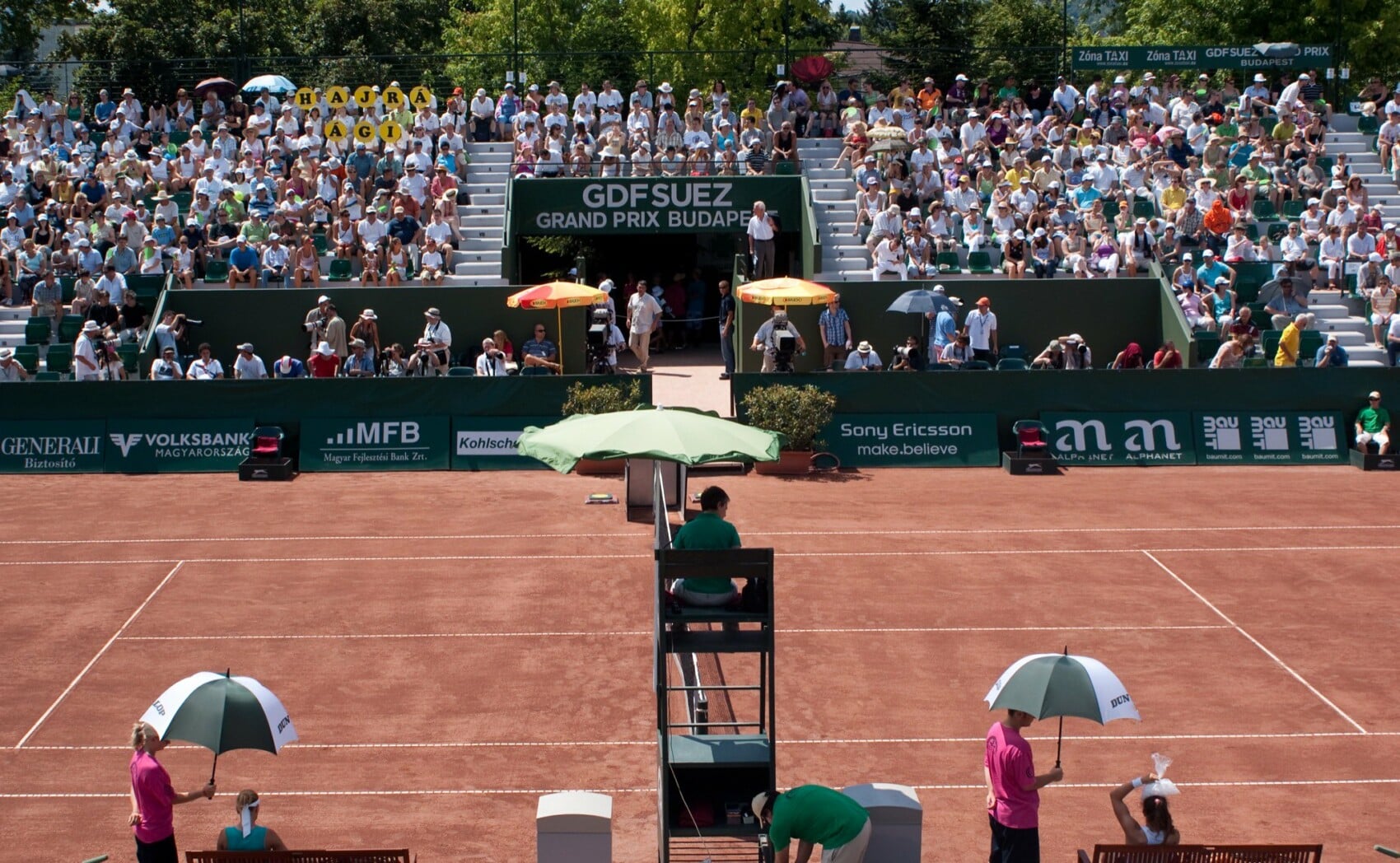Mecz tenisowy na kortach ziemnych GDF SUEZ Grand Prix Budapest – pełne trybuny kibiców, banery sponsorów, sędzia na podwyższeniu.