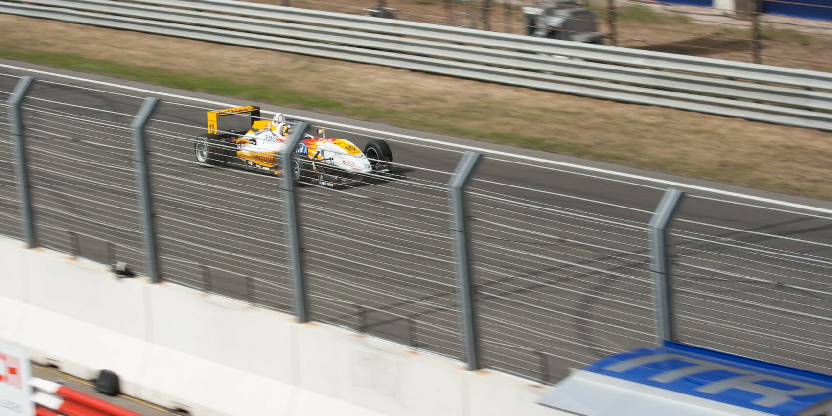 Bolid Formuły 3 na torze wyścigowym podczas wyścigu, widok z trybun, dynamiczne ujęcie motorsportu.