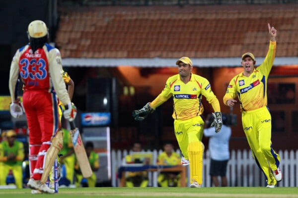 Zawodnicy cricketowi Chennai Super Kings w żółtych strojach świętują zdobycie wicket podczas meczu IPL przeciwko Royal Challengers Bangalore. Na pierwszym planie gracz w czerwonym stroju z numerem 333 odchodzi z boiska.