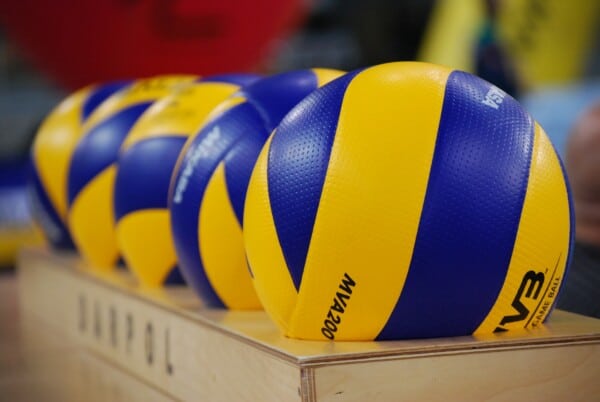 Oficjalne piłki siatkowe Mikasa MVA200 w kolorach żółto-niebieskich z logo FIVB ułożone w rzędzie na drewnianej powierzchni, używane w międzynarodowych turniejach siatkówki.