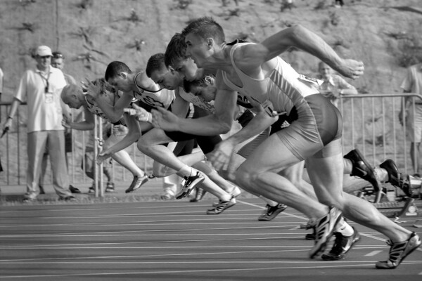 Zawodnicy rozpoczynający sprint na bieżni stadionu podczas zawodów lekkoatletycznych, dynamiczny moment startu wyścigu