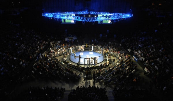 Widok z góry na oktagon podczas gali MMA, otoczony przez liczną publiczność i dynamiczne oświetlenie w arenie sportowej.