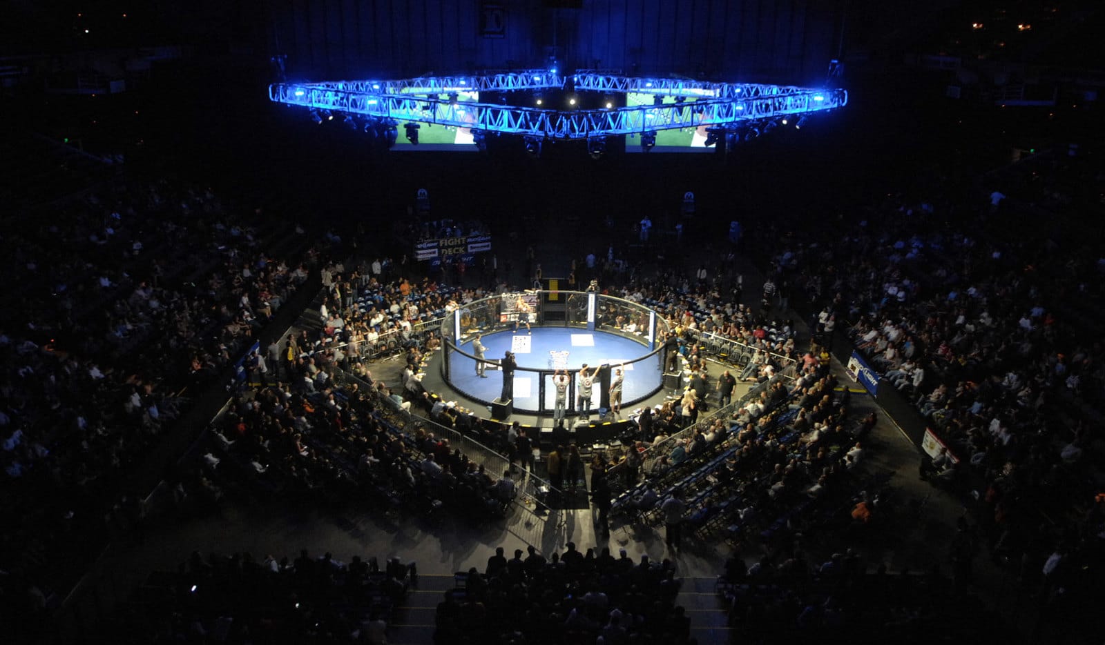 Widok z góry na oktagon podczas gali MMA, otoczony przez liczną publiczność i dynamiczne oświetlenie w arenie sportowej.