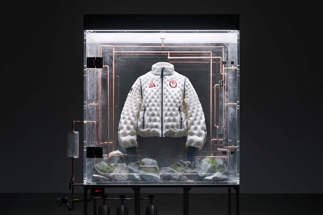 Biała kurtka Nike Therma-FIT Air Milano Team USA na Zimowe Igrzyska Olimpijskie 2026, prezentowana w futurystycznej gablocie.