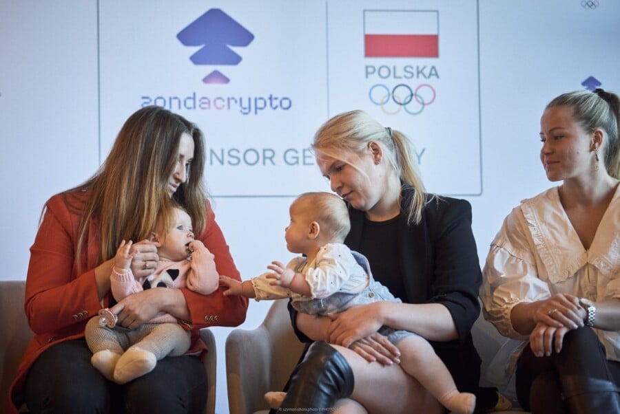 Dwie polskie olimpijki z dziećmi podczas konferencji programu Mamy Olimpijki PKOl i zondacrypto, na tle logotypów zondacrypto oraz Polskiego Komitetu Olimpijskiego.