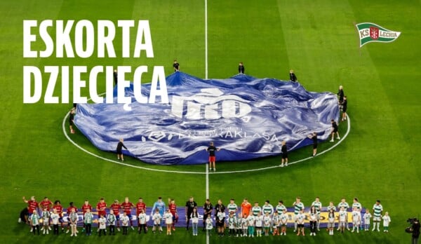 Dzieci w eskortach wyprowadzają piłkarzy Lechii Gdańsk na murawę podczas meczu Ekstraklasy, widoczny duży baner ligowy na środku boiska.