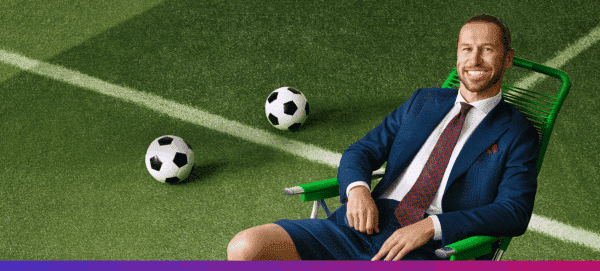 Grzegorz Krychowiak, polski piłkarz, siedzi w granatowym garniturze na zielonym leżaku na murawie boiska piłkarskiego, obok leżą piłki nożne.