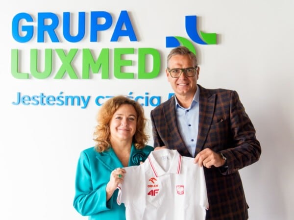 Przedstawiciele LUX MED prezentują koszulkę z logo Polskiego Związku Lekkiej Atletyki podczas oficjalnej współpracy, na tle logotypu GRUPA LUX MED.
