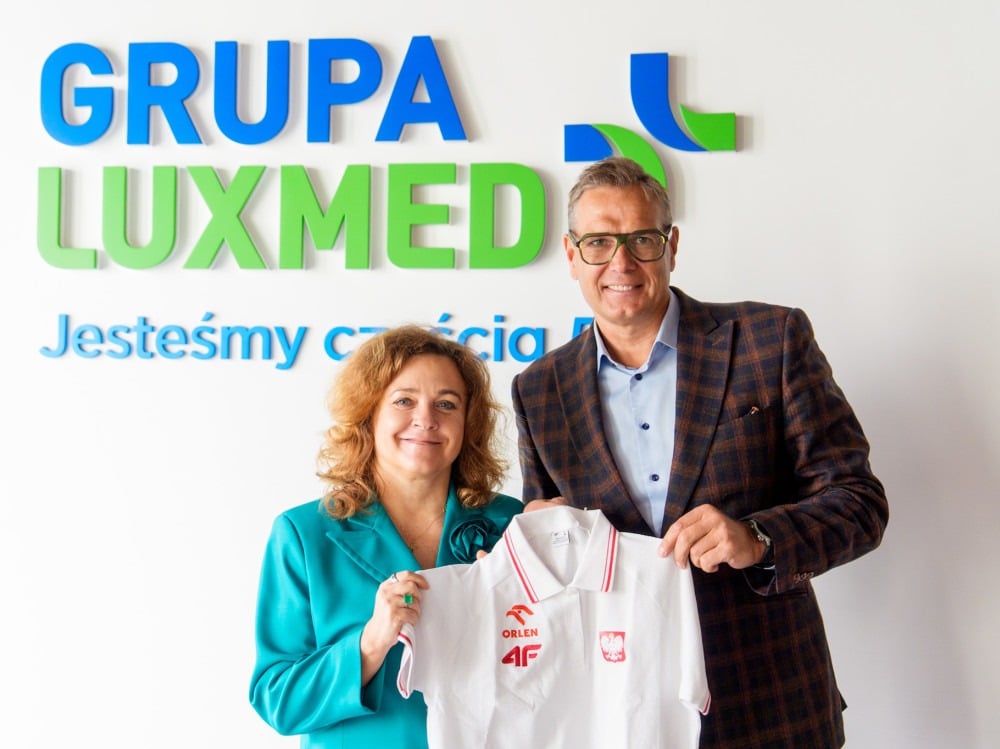 Przedstawiciele LUX MED prezentują koszulkę z logo Polskiego Związku Lekkiej Atletyki podczas oficjalnej współpracy, na tle logotypu GRUPA LUX MED.
