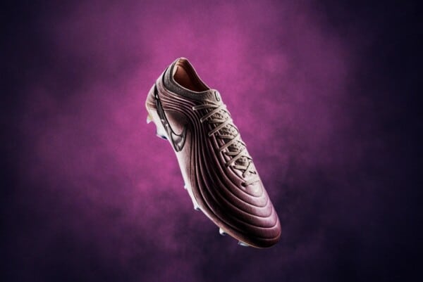 Korki piłkarskie Nike Tiempo Maestro Elite LE w purpurowo-fioletowym kolorze z cholewką Techleather, sznurowadłami i białym Swooshem Nike, unoszące się na fioletowym tle z mgłą i błyszczącymi korkami FG do twardej murawy.