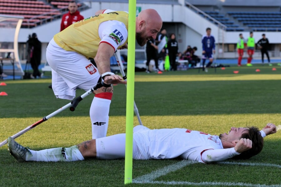 Polscy ampfutboliści w biało-czerwonych koszulkach świętują gola podczas finału International Challenge Cup w Tokio – zawodnik w żółtej koszulce u boku łysego gracza z protezą przy zielonej bramce, kibice Japonii na trybunach stadionu.