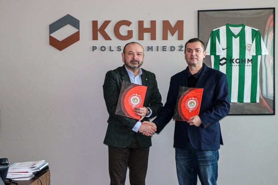 Prezes Zagłębia Lubin Paweł Jeż i Prezes Stowarzyszenia Muzeum Krzysztof Kostka podają sobie ręce, trzymając podpisane dokumenty na tle logotypu KGHM Polska Miedź.