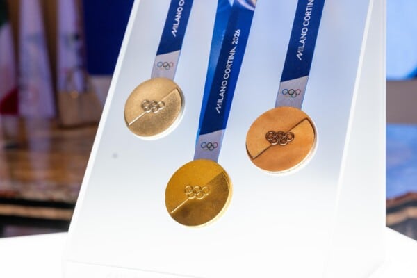 Zdjęcie oficjalnych medali Zimowych Igrzysk Olimpijskich Milano Cortina 2026 – złoty, srebrny i brązowy medal na niebiesko-białym stojaku z logo Milano Cortina 2026, symbolizujące osiągnięcia sportowców.