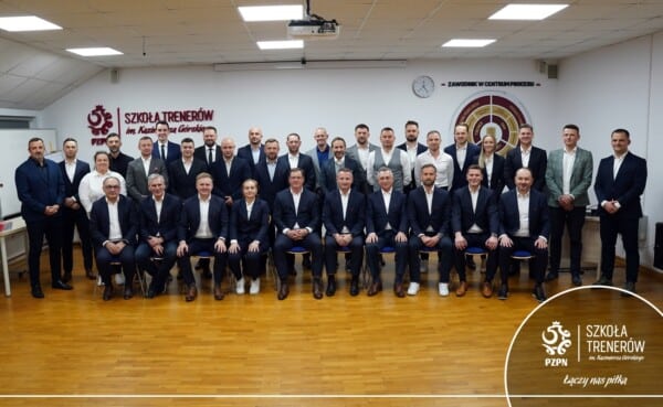 Grupowe zdjęcie 20 absolwentów kursu UEFA Pro 2024/2025 w Szkole Trenerów PZPN. Trenerzy w garniturach pozują przed logo PZPN i tarczą z napisem „Szkoła Trenerów”, w sali z zegarem i tablicą. Wśród nich Łukasz Piszczek i trenerzy Wisły Płock.