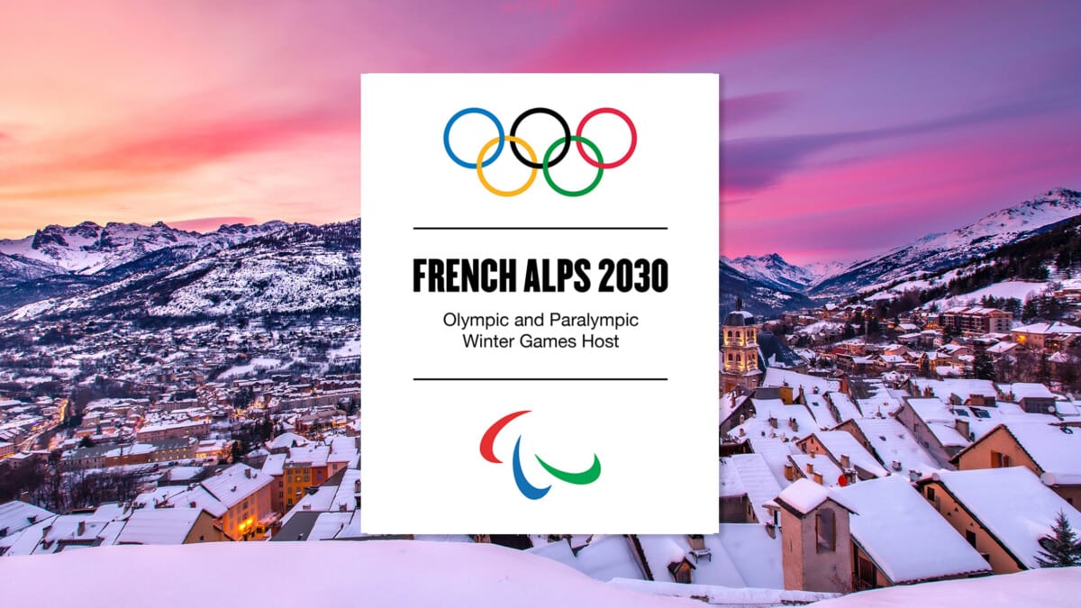 Grafika promocyjna Zimowych Igrzysk Olimpijskich i Paraolimpijskich 2030 we Francuskich Alpach z logo IOC i IPC, widokiem na zaśnieżone góry i miasto o zachodzie słońca