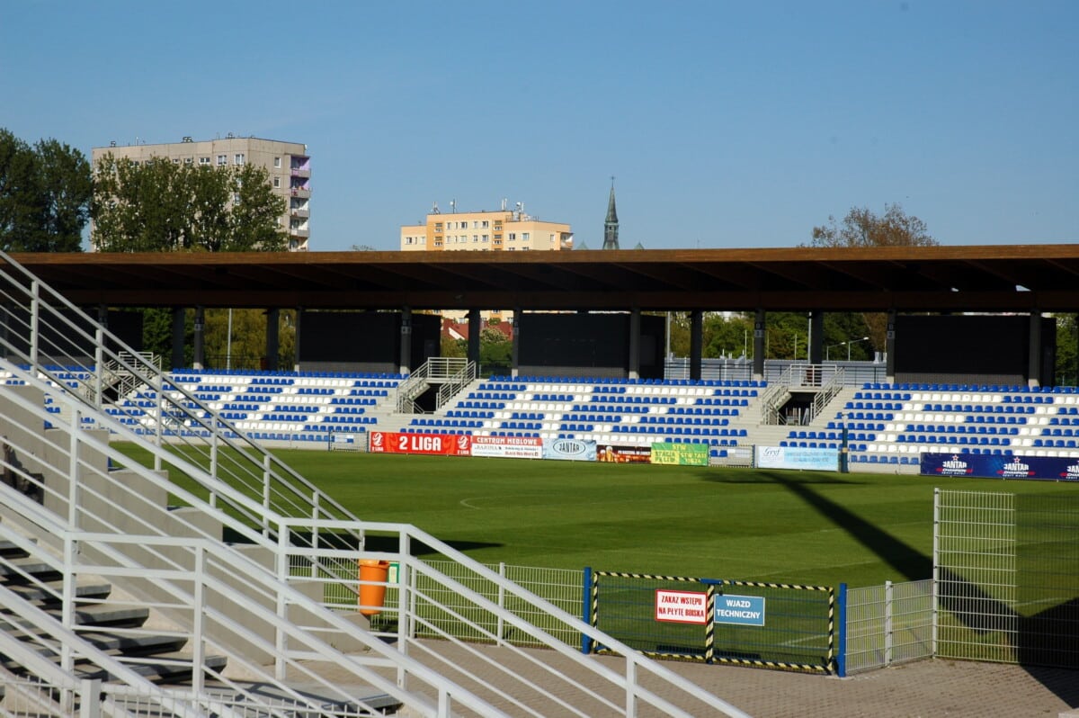 Zdjęcie stadionu miejskiego Kotwicy Kołobrzeg z trybuną wschodnią, boiska i otoczeniem – tu nowy MKS Kotwica walczy z decyzją FIFA o dziedziczeniu długów poprzednika.