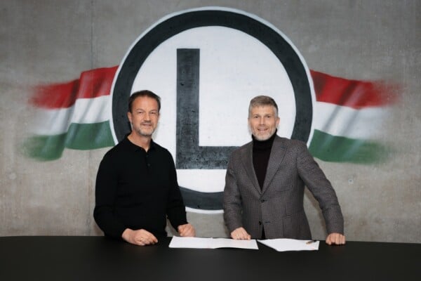 Bartłomiej Zalewski podpisuje umowę na tle herbu Legii Warszawa