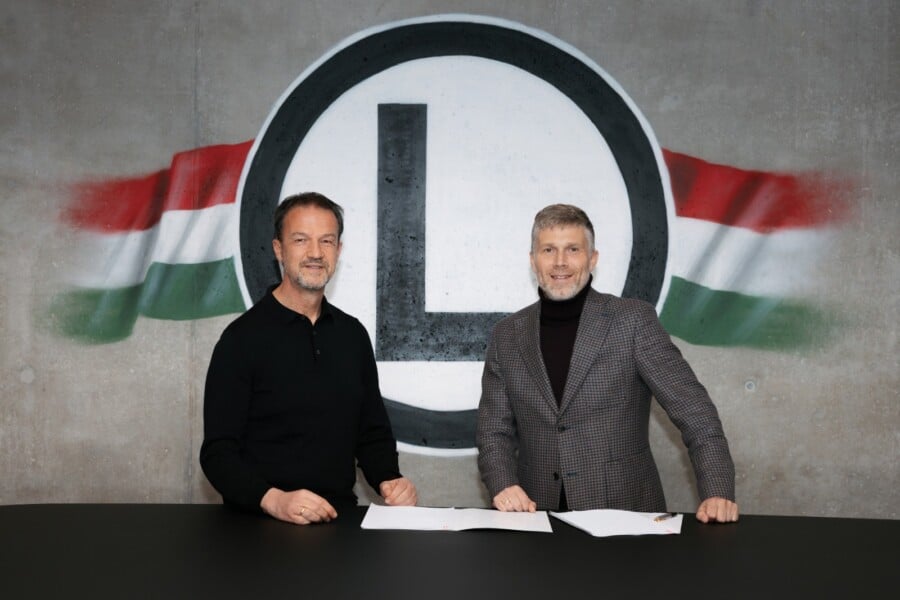 Bartłomiej Zalewski podpisuje umowę na tle herbu Legii Warszawa