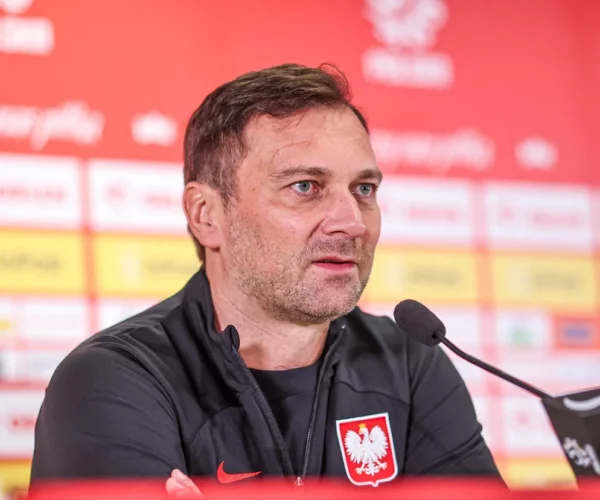 Jakub Kwiatkowski rzecznik prasowy reprezentacji Polski w piłce nożnej podczas konferencji prasowej. Odpowiada na pytania. Za nim znajduje się banda reklamowa.