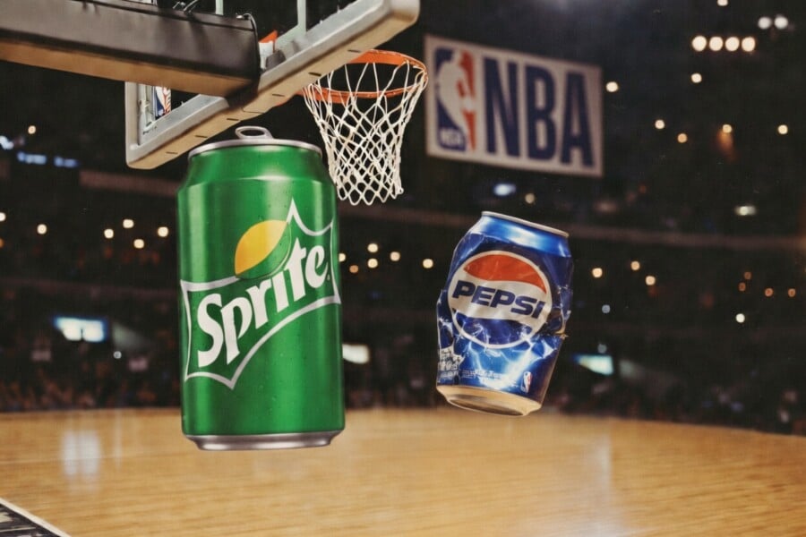 Zielona puszka Sprite i niebieska Pepsi w koszu NBA na tle parkietu z siatką i logo ligi – dynamiczna reklama napojów gazowanych w koszykówce.